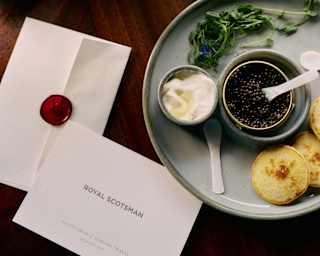 A plate of blinis, caviar and crème fraiche sits by an envelope with a broken wax seal and a card printed 'Royal Scotsman'.