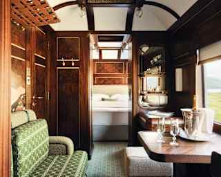 An emerald tweed banquette faces a window table where a Champagne cooler awaits, in a view through the Heron Grand Suite.