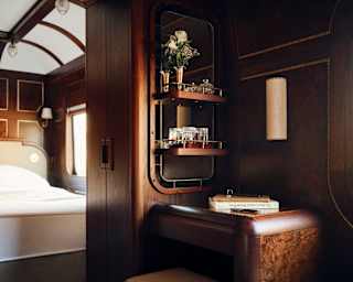View through the Heron Grand Suite, capturing a corner with glass shelves and a bedroom beyond, all encased in luxurious wood.