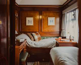 View of perpendicular single beds, seen through the doorway of a twin cabin filled with natural light from a window on the right.