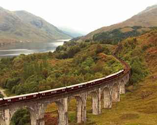 Aerial view of The Royal Scotsman as it crosses the Glenfinnan Viaduct on a damp and misty day, with views of Loch Shiel.