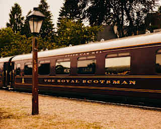 View of The Royal Scotsman's maroon carriages with gold lettering and white roof, seen past an old-fashioned street lamp.