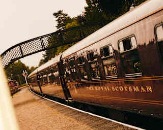 Angled image of The Royal Scotsman at a platform with a pedestrian bridge, seen from below a perpendicular sign for a museum.