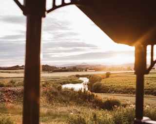A silver river snakes through fields as the sun glows on the horizon, seen from the Observation Car deck, framed by railings.