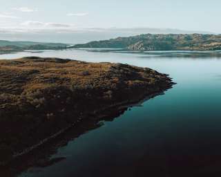 Still waters shimmer silvery-blue as they wrap around the heather-clad contours of a loch's banks in the Scottish Highlands.