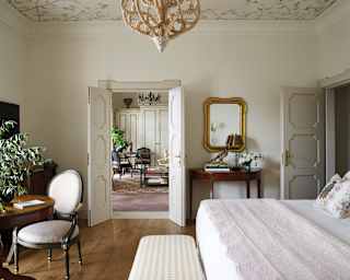 Light décor flows through a bedroom's double doors to a living room, where the wooden floor becomes luxurious carpet.