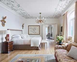 Two rococo wall mirrors, chandelier and period pieces marry with white bed and walls for fresh elegance in Miramare Suite.