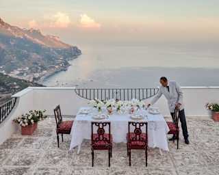 A staff member adds touches to a celebration table with white flowers and sublime coast views on Villa Margherita's terrace.