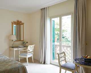 Elegant bedroom furniture nods to the Baroque with a gilt mirror and white curved leg chairs. Glass doors open onto a balcony