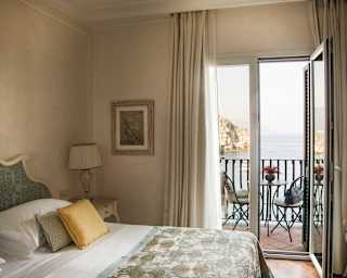 An elegant bedroom of soft creams and sage enjoys a private balcony with unrivalled views across the Bay of Mazzarò