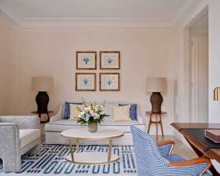 Four blue coral prints hang above a white sofa with cobalt detailing, flanked by lamps, in a room with a grey and blue chairs.
