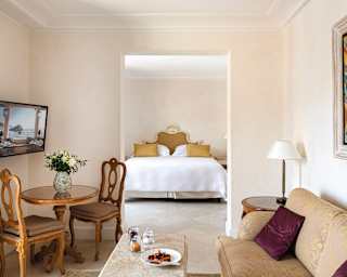 A sitting room with gold brocade sofa. Through an archway you can see a bedroom, the king bed topped with gold cushions
