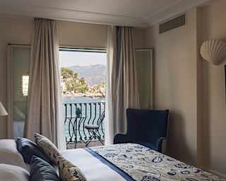 A ceramic pine cone sits on the balcony table. A botanic blue throw covers the bed end, matching the blue velvet chair