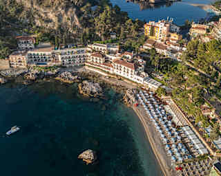 Stunning aerial view over Mazzarò beach, lined with lido parasols, and Villa San Andrea, tucked into the corner of the bay.