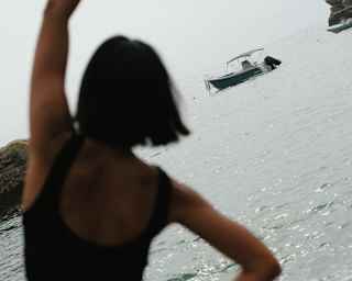 Angled image of a woman in a side bend as she does yoga on the beach, almost silhouetted against the sea, seen from behind.