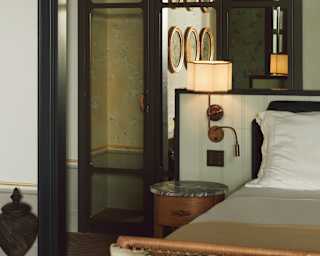 A mirrored wardrobe captures a reflection of artistic plates hanging on the wall behind the camera, in a view over the bed.