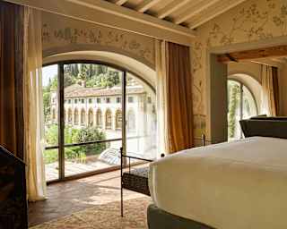 Glazed doors set into an arch bring views of the hotel into a calm bedroom with chinoiserie paper, cream décor and white bed.