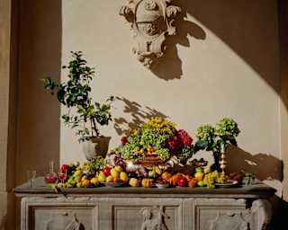 A stone altar-like table is adorned with a rainbow of produce including lemons, limes, pumpkins, grapes, cherries and flowers