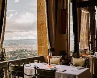 A restaurant table for four, with a white cloth and copper lamp, claims sublime views of Florence through a wide-open window.