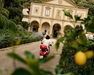 A man on a red vespa drives along the road towards Villa San Michele, in an angled shot taken from behind a lemon tree.