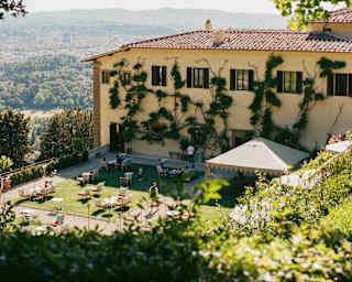 View down to the a large terrace where a gazebo and scattering of chairs sit on a lawn half-shaded by the hotel's shadow.