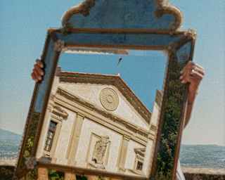 The pediment of Villa San Michele's front is reflected in a mirror which obscures the face of the person holding it, seen outside.