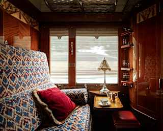 A teacup and teapot sit by a lamp on window table in a cosy Historic Cabin, in a view over a jacquard blue and red banquette.