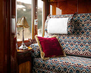 A large banquette in feather-pattern of blues and maroons and a plush red cushion catches light from the cabin window.