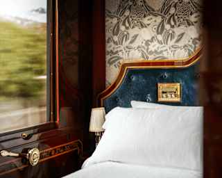 Embossed floral grey paper covers the wall behind the velvet navy headboard and white bed, seen in a Venice Suite detail.