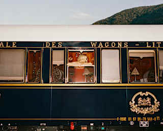A blonde woman leans on an open carriage window, head turned to the side, in an exterior view of the black and white train.