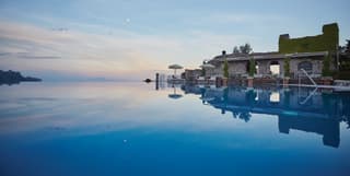 An infinity pool, with reflections of flowers and wall, disappears into an horizonless sky with ribbons of palest sunset pink
