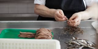 Lady in a black apron preparing anchovy fish in a factory kitchen