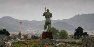 Giant bronze statue of a warrior among a field of poppies and scattered rocks in Pompeii