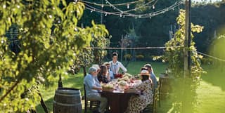 A large family dine together in the garden at a long table between ancient vines. An old wine barrel acts as a side table
