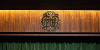 A brass plaque featuring the cut-out curlicues of the Copacabana Palace Hotel monogram hangs above the theatre stage