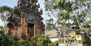 Ornate-tiered stone temple pagoda surrounded by shrubs and palm trees
