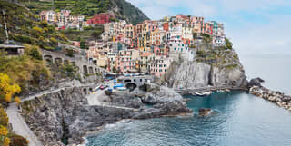 The tiny, picturesque Cinque Terre town of Manarola, with pastel buildings clinging to a rock above a small azure harbour.