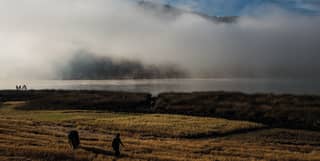 As day breaks, a man and his horse walk through farmland and mist rises from Huaypo lake behind, obscuring the hills and sky.