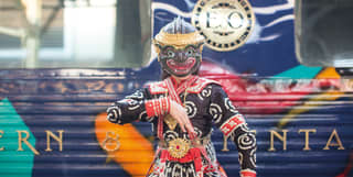 Dancer in a traditional Thai lion mask posing in front of train carriages