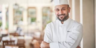 Michelin-starred executive chef, the native Sicilian Roberto Toro, smiles at the camera in his chef's whites and toque hat