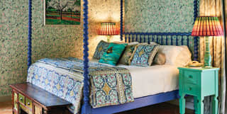 Indigo blue four-poster king-bed in a hotel room with vibrant floral wallpaper