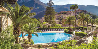 Outdoor hotel pool surrounded by palm trees overlooking the Tramuntana mountains