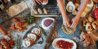Hands kneading dough on a kitchen counter topped with various pastries