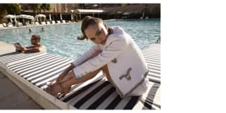 Lily-Rose Depp poses on the poolside cushion seating in high heels and a white jacket by Chanel, with embroidery detail.