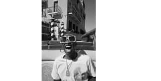 Black and white image of actress-singer, Cynthia Erivo in big dark glasses, laughing in a water taxi outside the hotel.