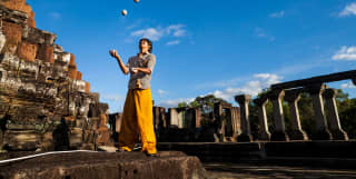 Amid the ruins of a Cambodian temple, a juggler carefully watches three balls in the air