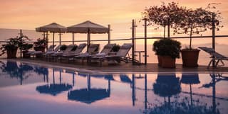 Hotel infinity pool surrounded by potted plants and sunbeds at sunset