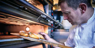 Acclaimed chef, Benoit Blin, checks the texture of freshly cooked pastries as he uses a wooden pizza paddle to remove them