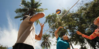 View from underneath a volleyball net of three players reaching for a ball