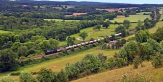 The black body of the steam engine pulls cream and burgundy carriages through a perfect lush English countryside